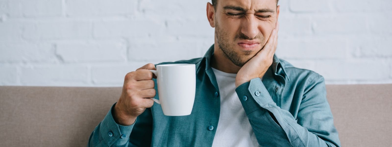 Man suffering from a tooth ache while holding a coffee mug with one hand.